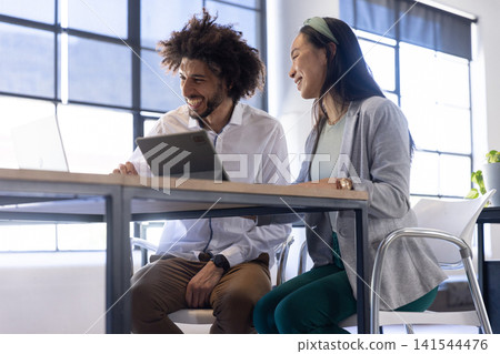 Middle eastern male colleagues collaborating on tablet at office desk near potted plant, laptop Middle eastern male colleagues collaborating on tablet at office desk near potted plant, laptop 141544476