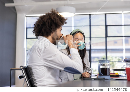 Diverse coworkers sipping coffee from mugs at table with french press, pastries Diverse coworkers sipping coffee from mugs at table with french press, pastries 141544478