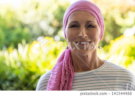 Senior woman standing, smiling in garden wearing headscarf, striped shirt, dangling earrings 141544488