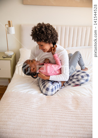African american mother with daughter hugging and laughing on bed in bedroom with tufted headboard African american mother with daughter hugging and laughing on bed in bedroom with tufted headboard 141544528
