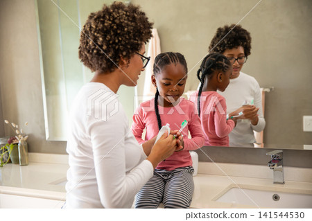 Diverse mother and daughter brushing teeth at home bathroom sink using toothbrushes 141544530
