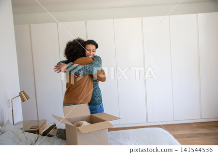 Diverse family hugging in bedroom near moving box on gray bedding with brass lamp and smartphone Diverse family hugging in bedroom near moving box on gray bedding with brass lamp and smartphone 141544536