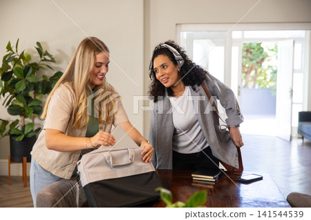 Diverse coworkers packing tablet into grey backpack at table next to open glass doors, copy space Diverse coworkers packing tablet into grey backpack at table next to open glass doors, copy space 141544539