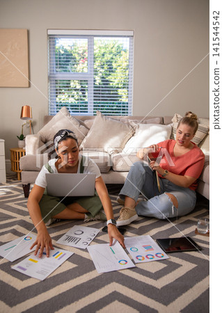Diverse female friends studying charts, knitting yarn on zigzag rug with laptop in living room Diverse female friends studying charts, knitting yarn on zigzag rug with laptop in living room 141544542