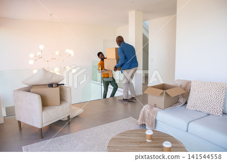 African american father, son handing stacked cardboard boxes at home loft with glass railing African american father, son handing stacked cardboard boxes at home loft with glass railing 141544558
