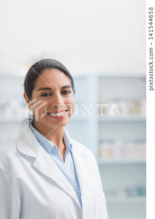 Female pharmacist standing in clinic with shelving medication boxes wearing white lab coat smiling 141544658