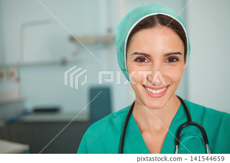 Female nurse smiling toward camera in clinic wearing green scrubs and surgical cap with stethoscope 141544659