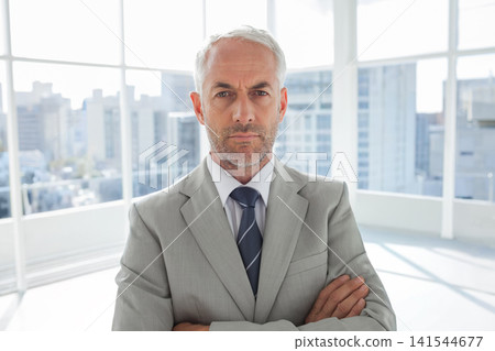 50s man standing arms crossed, facing camera in office windows in light-gray suit and striped tie 50s man standing arms crossed, facing camera in office windows in light-gray suit and striped tie 141544677