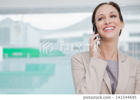 Businesswoman holding smartphone to ear, smiling and talking at office window with pool, copy space Businesswoman holding smartphone to ear, smiling and talking at office window with pool, copy space 141544695