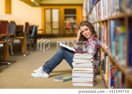 Woman reading open book on library carpet, leaning against shelves, books beside, copy space Woman reading open book on library carpet, leaning against shelves, books beside, copy space 141544719
