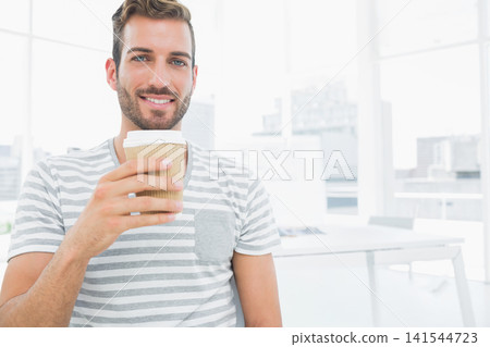 Man wearing gray striped tee holding ribbed disposable coffee cup in bright modern office Man wearing gray striped tee holding ribbed disposable coffee cup in bright modern office 141544723