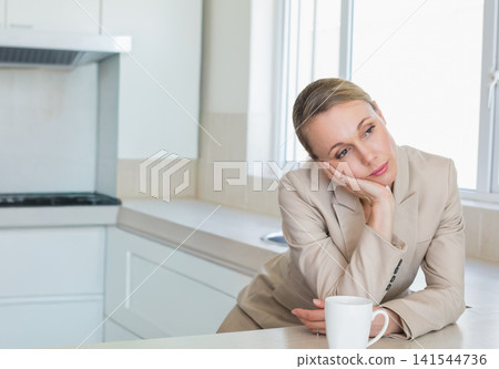 Mid adult woman wearing blazer leaning on counter in kitchen, resting head, ceramic mug, copy space Mid adult woman wearing blazer leaning on counter in kitchen, resting head, ceramic mug, copy space 141544736