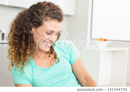 Adult woman wearing mint T-shirt smiling, looking down right in kitchen with fruit bowl, copy space Adult woman wearing mint T-shirt smiling, looking down right in kitchen with fruit bowl, copy space 141544739