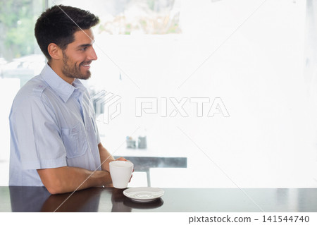 Adult man standing at cafe counter holding white mug, wearing light blue shirt, looking, copy space 141544740