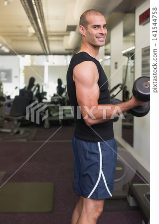 Adult male performing biceps curl using dumbbell at gym, wearing black top and navy shorts Adult male performing biceps curl using dumbbell at gym, wearing black top and navy shorts 141544758