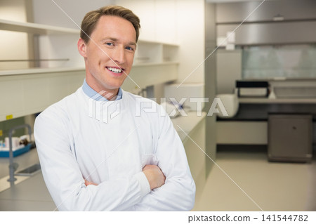 Male adult wearing white lab coat standing with arms crossed in clinical laboratory bench with hood Male adult wearing white lab coat standing with arms crossed in clinical laboratory bench with hood 141544782