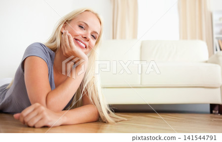 Female lying on hardwood floor in living room, smiling, wearing grey top near sofa, copy space Female lying on hardwood floor in living room, smiling, wearing grey top near sofa, copy space 141544791