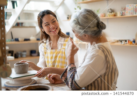 Happy Asian Mother and Daughter Talking and Smiling in Pottery workshop at cozy studio Happy Asian Mother and Daughter Talking and Smiling in Pottery workshop at cozy studio 141544870
