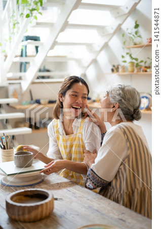 Senior Mother Touching Laughing Daughter's Face during a Pottery Class in art workshop. 141544871