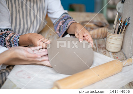 Close Up of Senior Woman Hands Holding Flat Clay Disc for Plate Making in pottery workshop studio 141544906