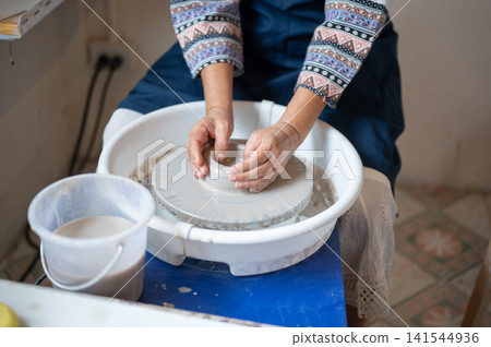 High Angle View of Senior Woman Hands Centering Clay on Potter's Wheel in pottery workshop studio. High Angle View of Senior Woman Hands Centering Clay on Potter's Wheel in pottery workshop studio. 141544936