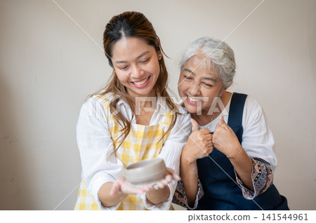 Asian Mother and Daughter Smiling and Giving Thumbs Up with Clay Bowl in pottery workshop studio. 141544961