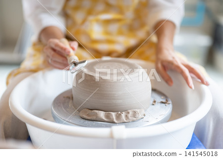 Close Up of Woman Hand s Trimming Inverted Clay Bowl Base with Loop Tool in pottery workshop studio. Close Up of Woman Hand s Trimming Inverted Clay Bowl Base with Loop Tool in pottery workshop studio. 141545018