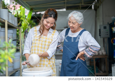 Asian Mother and Daughter Smiling while Glazing Ceramic Bowl Together in pottery workshop Asian Mother and Daughter Smiling while Glazing Ceramic Bowl Together in pottery workshop 141545029