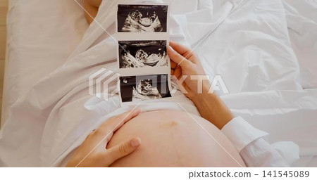 Pregnant woman holding ultrasound images on bed Pregnant woman holding ultrasound images on bed 141545089