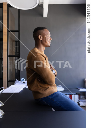 African american man sitting on office desk in workspace showing document stacks, copy space African american man sitting on office desk in workspace showing document stacks, copy space 141545306