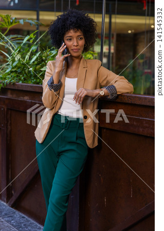 African american woman leaning by wooden planter at office lobby talking on smartphone African american woman leaning by wooden planter at office lobby talking on smartphone 141545332