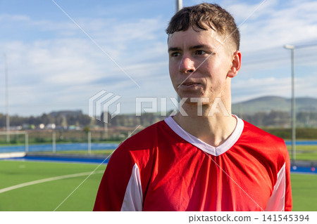 Male athlete in red jersey standing on turf field gazing left toward goal posts, copy space Male athlete in red jersey standing on turf field gazing left toward goal posts, copy space 141545394