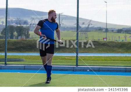Male athlete running and holding field hockey stick dribbling ball on turf field Male athlete running and holding field hockey stick dribbling ball on turf field 141545396