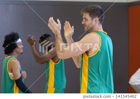 Diverse male teammates in jerseys clapping during practice at gym, copy space Diverse male teammates in jerseys clapping during practice at gym, copy space 141545402