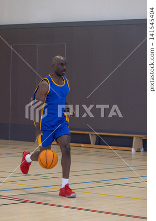 African american man in blue and yellow uniform dribbling basketball across gym floor African american man in blue and yellow uniform dribbling basketball across gym floor 141545404