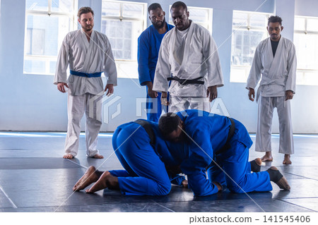 Two african american men grappling on padded mats in training hall in blue gis black belts Two african american men grappling on padded mats in training hall in blue gis black belts 141545406