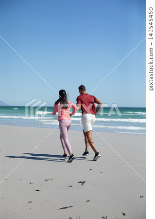 Friends jogging along sandy beach shoreline in running shoes, securing hair with hair tie Friends jogging along sandy beach shoreline in running shoes, securing hair with hair tie 141545450