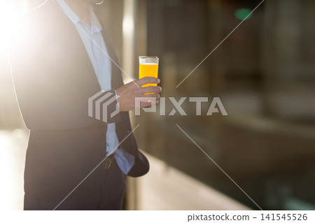 Midadult man in dark suit shirt standing holding orange juice glass in office lobby, copy space Midadult man in dark suit shirt standing holding orange juice glass in office lobby, copy space 141545526
