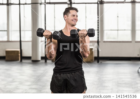Male wearing black tank top and shorts in gym holding hex dumbbells performing biceps curls Male wearing black tank top and shorts in gym holding hex dumbbells performing biceps curls 141545536