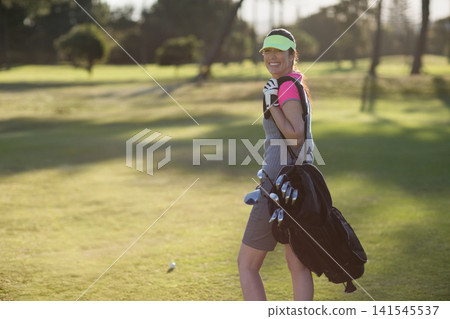 Female golfer walking on fairway carrying golf bag with clubs and wearing neon visor, copy space Female golfer walking on fairway carrying golf bag with clubs and wearing neon visor, copy space 141545537