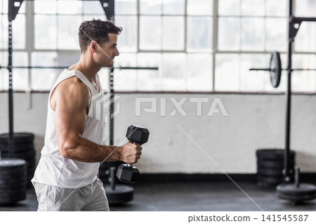 Man late 20s standing in gym holding hex dumbbell by squat rack, wearing tank, copy space Man late 20s standing in gym holding hex dumbbell by squat rack, wearing tank, copy space 141545587