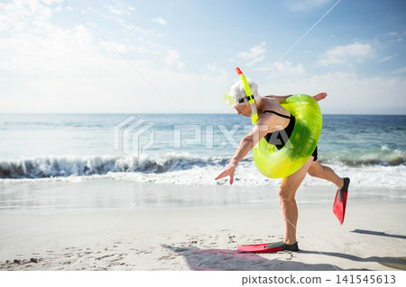 Senior female wearing black swimsuit, snorkel mask, float and fins, balancing on shore, copy space Senior female wearing black swimsuit, snorkel mask, float and fins, balancing on shore, copy space 141545613