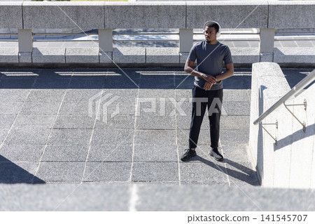 African American man standing on open paved terrace wearing athletic tee and headphones, copy space African American man standing on open paved terrace wearing athletic tee and headphones, copy space 141545707