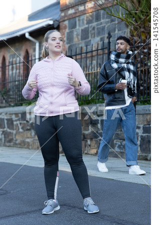 Diverse pedestrians pausing during workout on sidewalk by stone wall, showing wireless earphones Diverse pedestrians pausing during workout on sidewalk by stone wall, showing wireless earphones 141545708