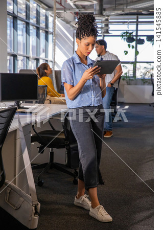Diverse coworkers working while African American woman holding tablet in open office near monitors 141545885