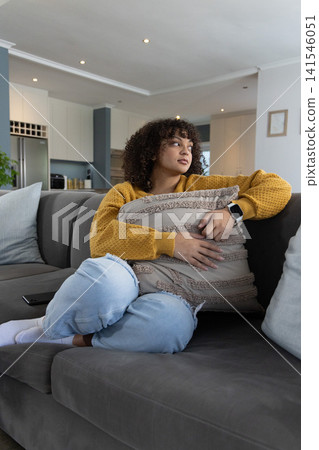 African American woman on sofa hugging throw in mustard top, checking smartwatch near phone at home African American woman on sofa hugging throw in mustard top, checking smartwatch near phone at home 141546051