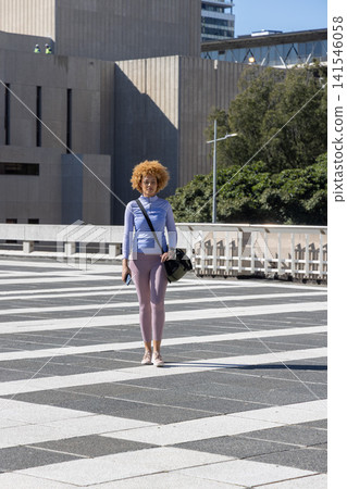 African American woman in her 20s standing on patterned plaza holding smartphone and bag African American woman in her 20s standing on patterned plaza holding smartphone and bag 141546058