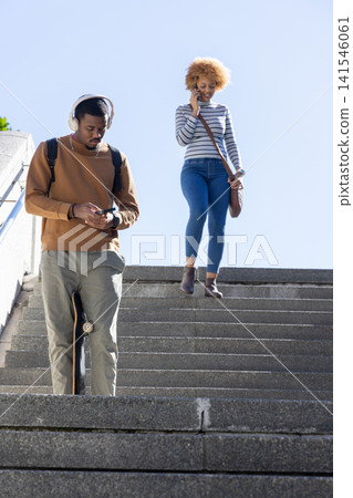African American man and woman descending steps, man holding skateboard, woman speaking on phone African American man and woman descending steps, man holding skateboard, woman speaking on phone 141546061