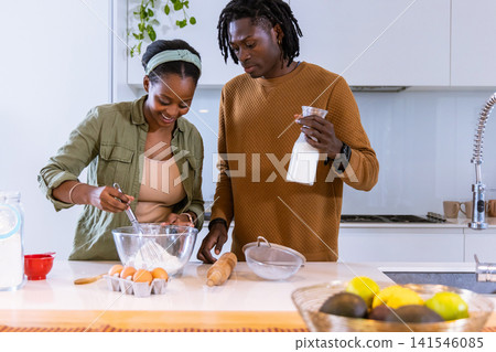 African American couple whisking batter in home kitchen using whisk, glass bowl, milk bottle, eggs African American couple whisking batter in home kitchen using whisk, glass bowl, milk bottle, eggs 141546085