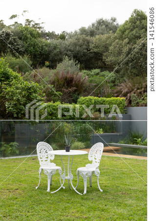 White ornate bistro table and chairs sitting on manicured lawn in backyard with potted succulent White ornate bistro table and chairs sitting on manicured lawn in backyard with potted succulent 141546086